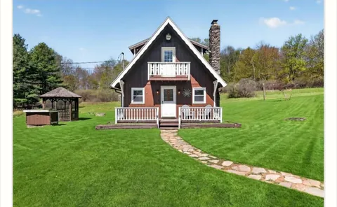 Before: the same chalet with red siding, a white porch rail and an open lawn